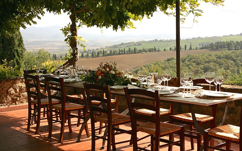 Table set for al fresco dinner overlooking a view of a hill in Tuscany.