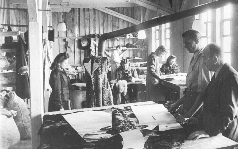 A black-and-white photograph of the furrier Bennewitz family in Wurzen, Germany, taken around 1951 or 1952. Pictured are three women and three men working on various fur garments.