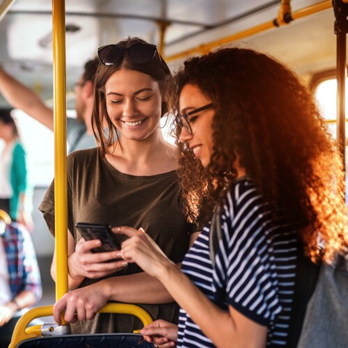One woman showing a phone to another on a bus.