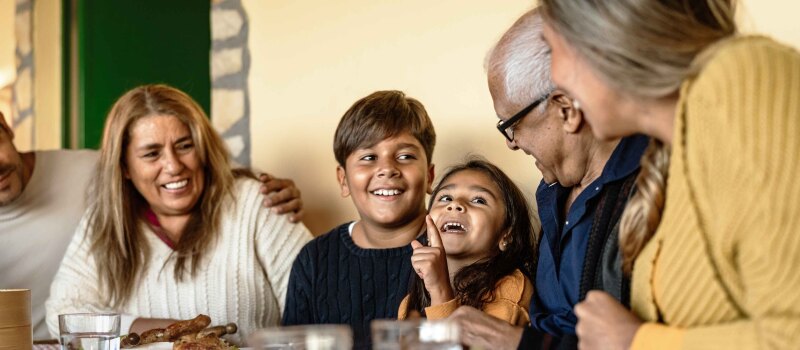 Trois générations d'une famille latino-américaine discutant et souriant à table.