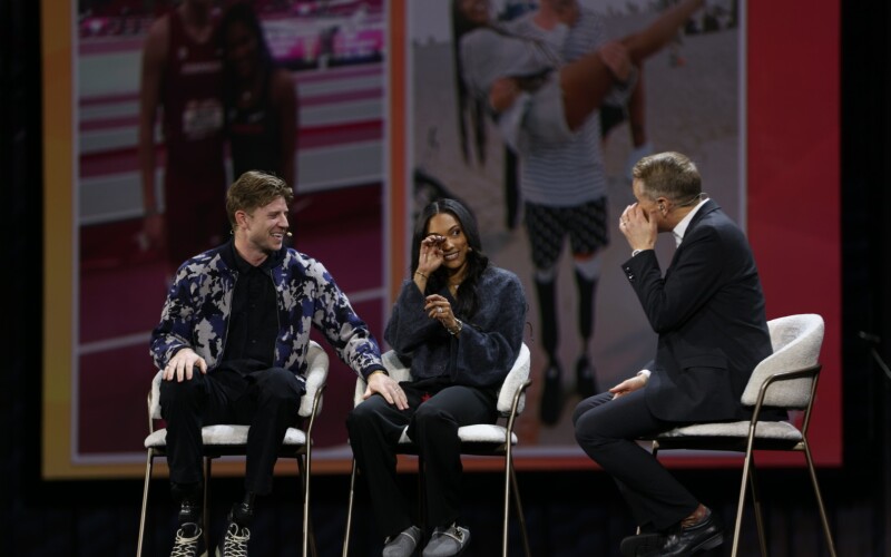 Tara Davis-Woodhall y Hunter Woodhall se sientan en el escenario principal de RootsTech con Kirby Heyborne