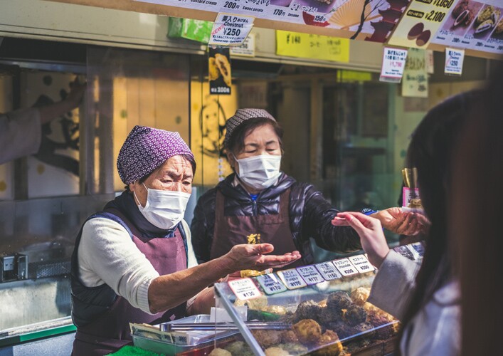 two women wear face coverings as they sell food.