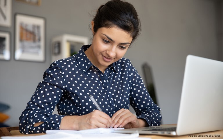 Woman taking notes while at a computer.