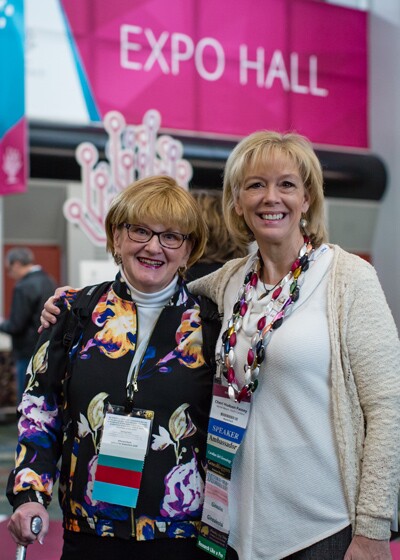 Two women standing in front of the RootsTech Expo Hall.