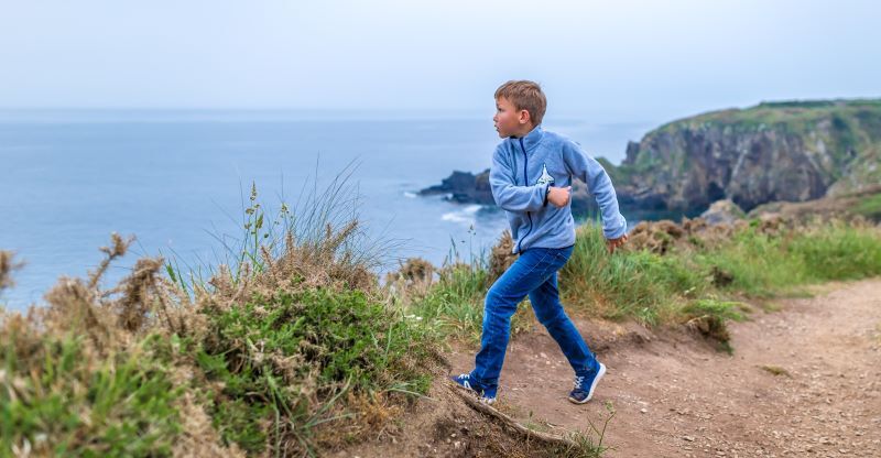 A young boy running along a cliffside in Wales