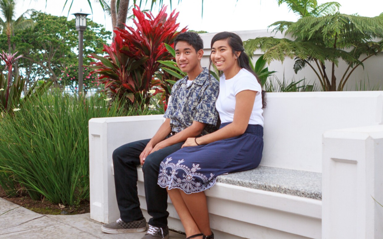 Young man and young woman sitting on a bench on temple grounds.
