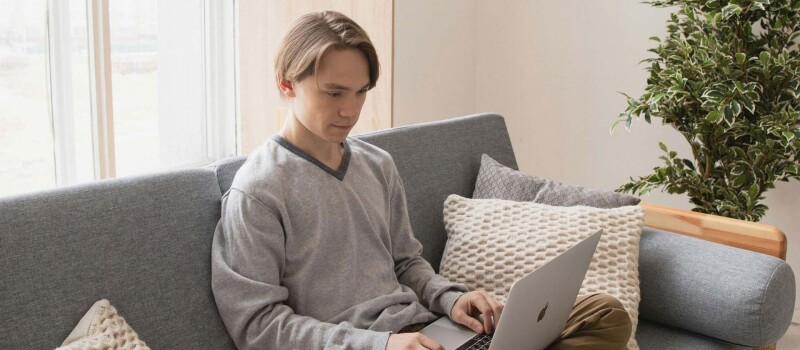 A young man looking at a laptop while sitting on a couch.