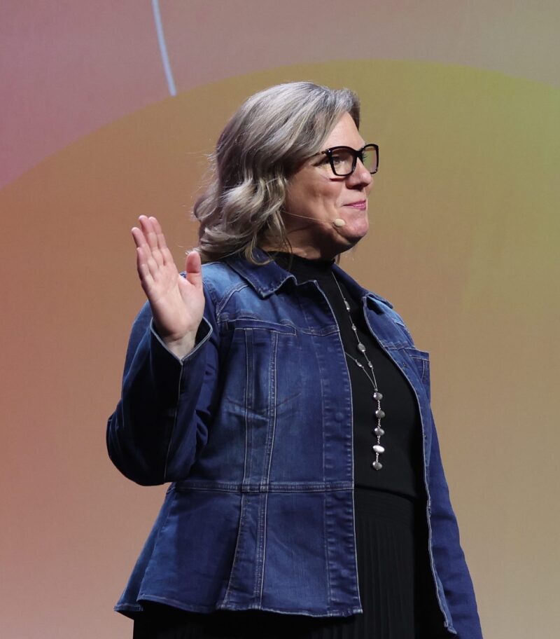 Dr. Jody Koenig Kellas vinker til publikum fra presentasjonsscenen på RootsTech.