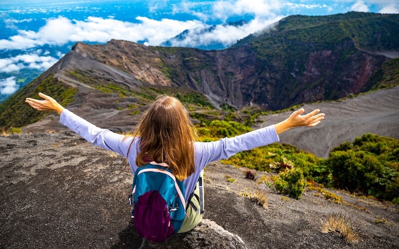 Girl with backpack sits on top of a volcano in Costa Rica
