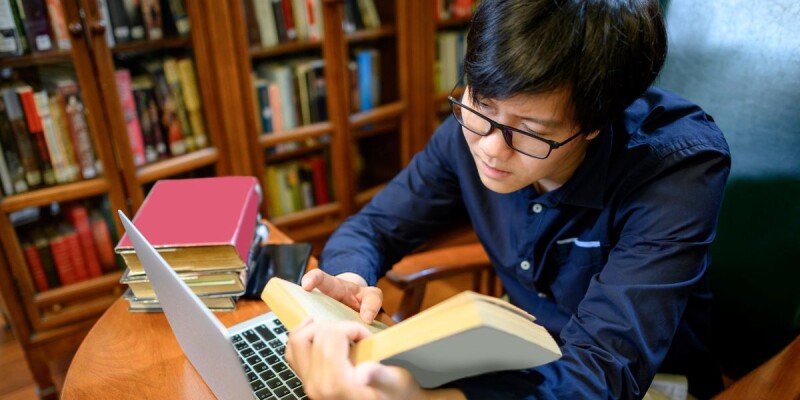 A young Asian man studies in a library.