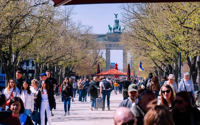 Turisták egy csoportja sétál egy berlini utcán, a háttérben a Brandenburgi kapuval