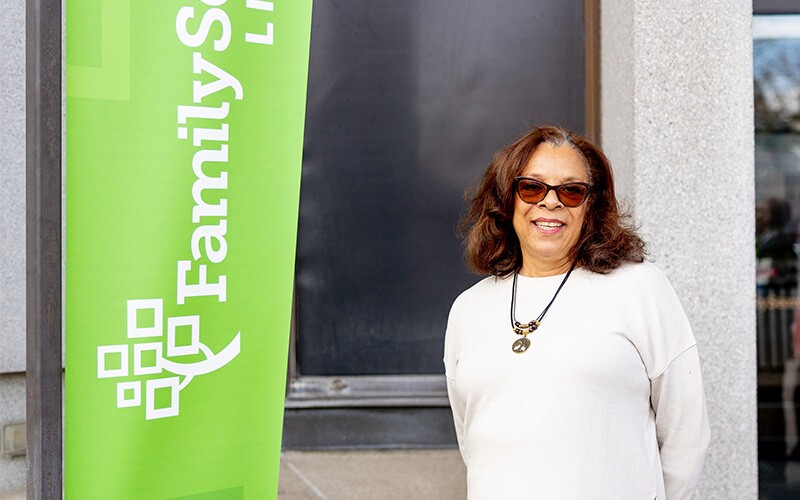 A smiling woman stands in front of a sign that says "FamilySearch Library."