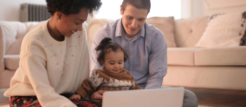 A couple with their baby between them, looking at a laptop together.