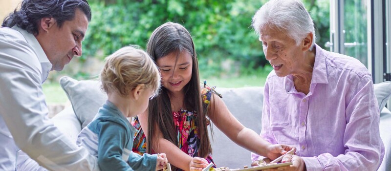 A young boy and girl smiling and playing with a block puzzle while 2 adults watch.