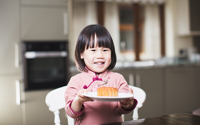 A little Asian girl smiles while holding out a mooncake