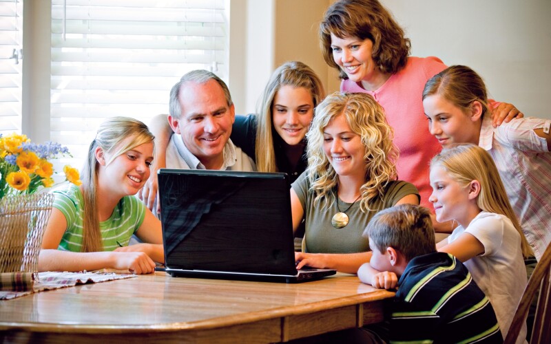 A family sitting around a table and looking at a laptop screen together.