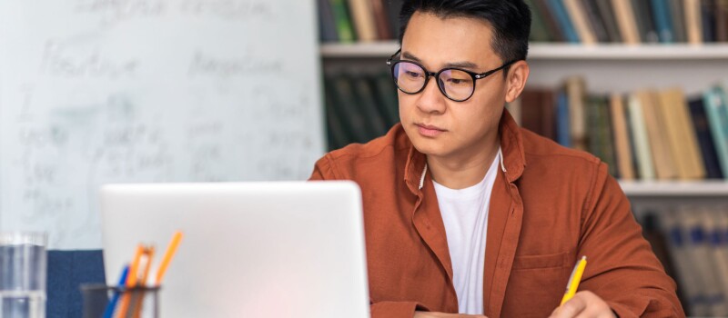 A Korean man highlighting his handwritten notes while looking at a laptop screen.