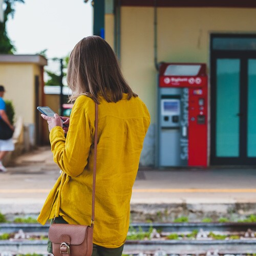 Woman waiting for a train and doing family history on her cell phone.