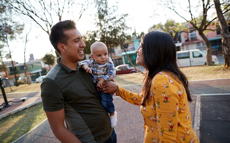 A husband holds his son and smiles at his wife.