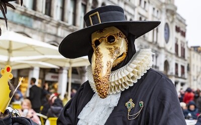 En person på karnevalet i Venezia kledd i kostyme og iført en dekorert pestlege-maske