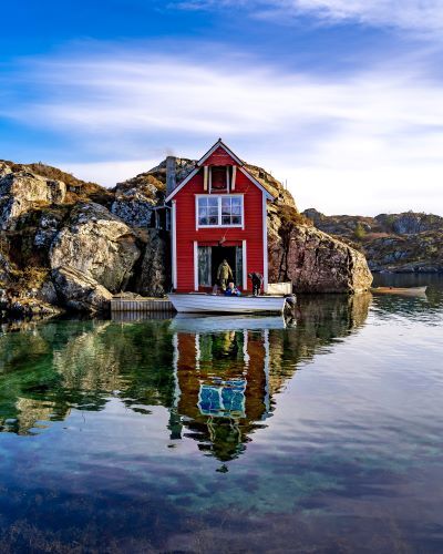 A red boathouse on the edge of a blue lake in Sweden